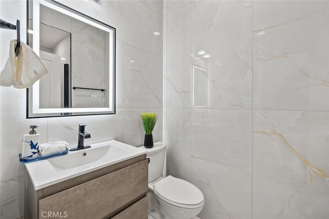 bathroom with toilet, vanity, and tile walls