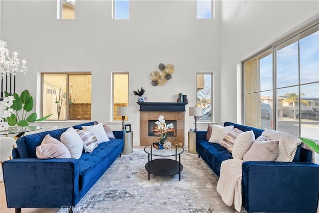 living area featuring a tile fireplace, an inviting chandelier, a towering ceiling, and a wealth of natural light