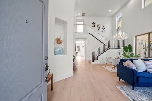 foyer featuring light wood-type flooring, baseboards, a towering ceiling, a notable chandelier, and stairs