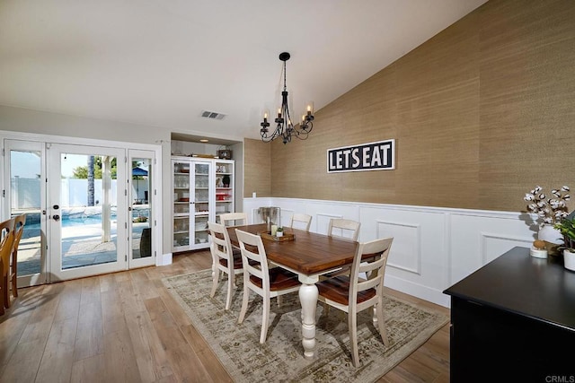 dining space featuring vaulted ceiling, visible vents, a wainscoted wall, and an inviting chandelier