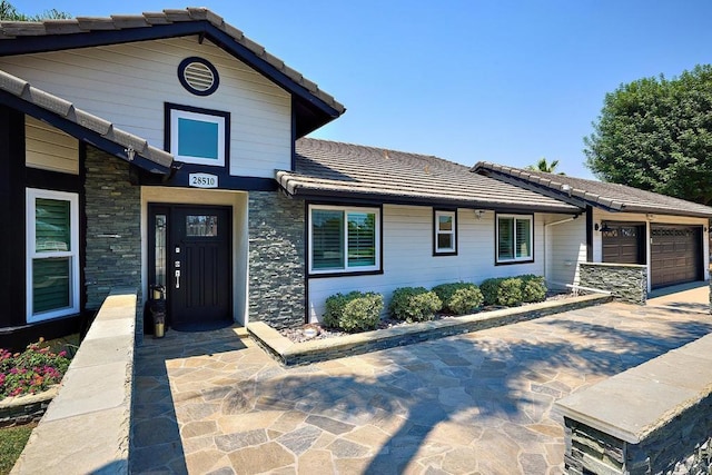 view of front facade featuring an attached garage, driveway, stone siding, and a tiled roof