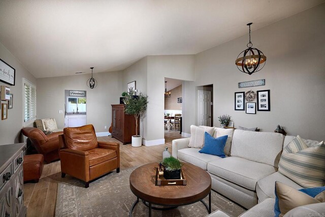 living area featuring baseboards, lofted ceiling, a chandelier, and light wood-type flooring