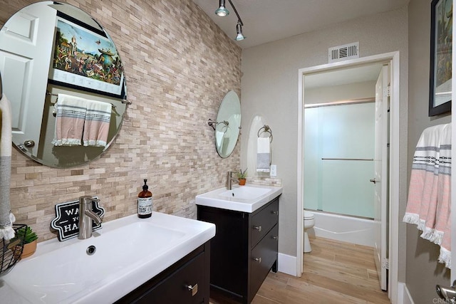 bathroom with shower / bath combination with glass door, wood finished floors, a sink, and visible vents