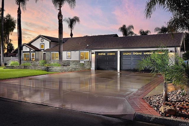 view of front facade with an attached garage, a tiled roof, driveway, and stone siding