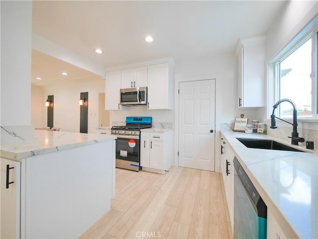 kitchen with white cabinetry, stainless steel appliances, light stone counters, and a sink