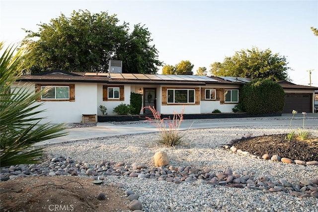 ranch-style home featuring roof mounted solar panels, driveway, and stucco siding
