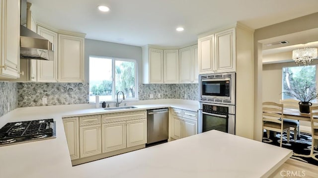 kitchen with backsplash, light countertops, a sink, wall chimney exhaust hood, and appliances with stainless steel finishes