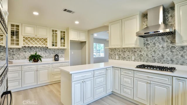 18971 Birch St, Perris, CA 92570 - kitchen with wall chimney exhaust hood, stainless steel gas cooktop, light wood finished floors, tasteful backsplash, and a peninsula