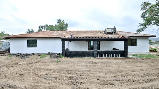 rear view of property with stucco siding, a tiled roof, and central AC unit