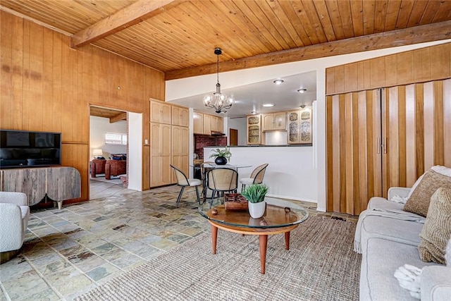 living room with wooden walls, wood ceiling, stone tile flooring, a notable chandelier, and beam ceiling