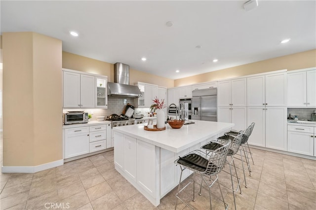 kitchen with tasteful backsplash, stainless steel appliances, wall chimney exhaust hood, and white cabinets