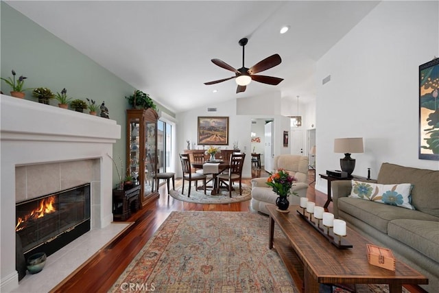 living room with a tile fireplace, lofted ceiling, a ceiling fan, visible vents, and wood finished floors