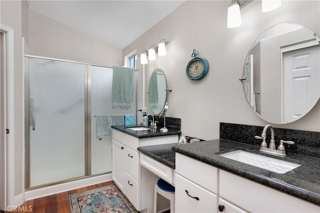 full bath featuring a stall shower, two vanities, wood finished floors, and a sink