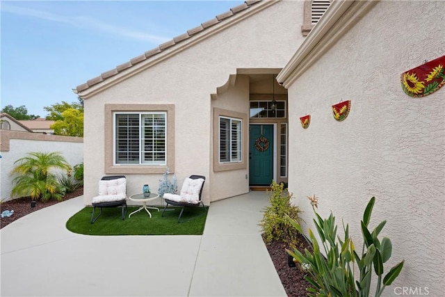 view of exterior entry featuring fence, stucco siding, and a patio area