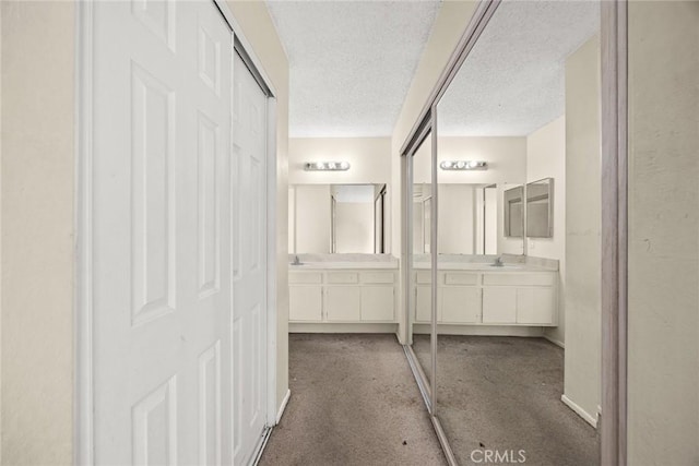hall featuring carpet floors, a textured ceiling, baseboards, and a sink