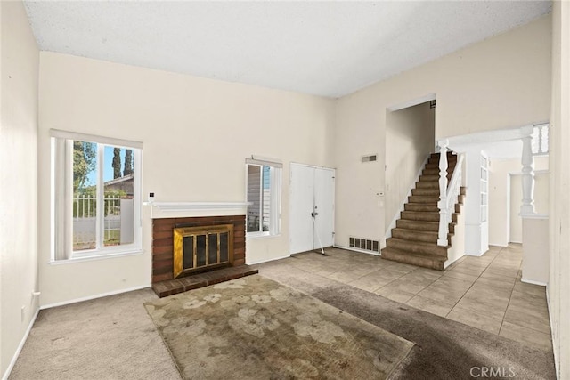unfurnished living room featuring tile patterned flooring, visible vents, baseboards, a brick fireplace, and stairs