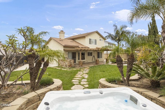 back of house with a chimney, an outdoor hot tub, fence, a yard, and stucco siding