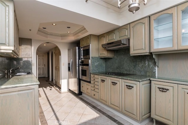 kitchen with a sink, decorative backsplash, arched walkways, stainless steel appliances, and under cabinet range hood
