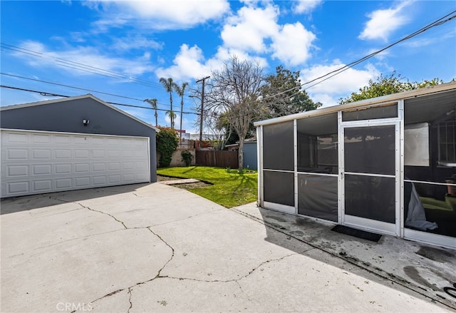view of patio / terrace with a detached garage, an outbuilding, a sunroom, and fence
