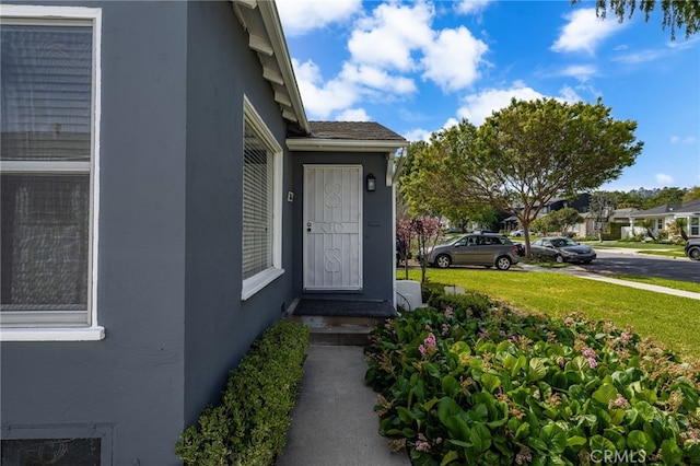doorway to property with a lawn and stucco siding