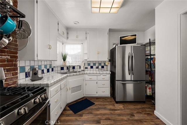 kitchen with appliances with stainless steel finishes, tile counters, a sink, and white cabinetry