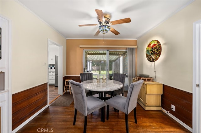 dining room with ornamental molding, ceiling fan, dark wood-style flooring, and a wainscoted wall