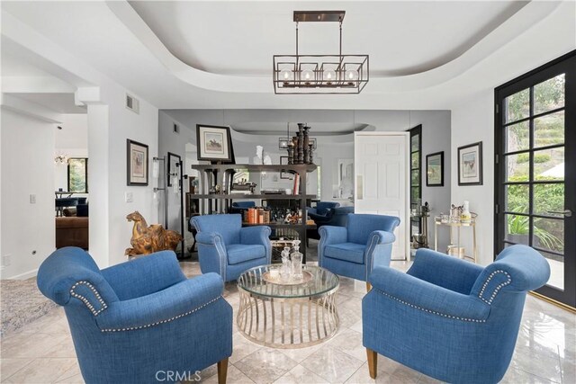 living area with a raised ceiling, visible vents, a chandelier, and plenty of natural light