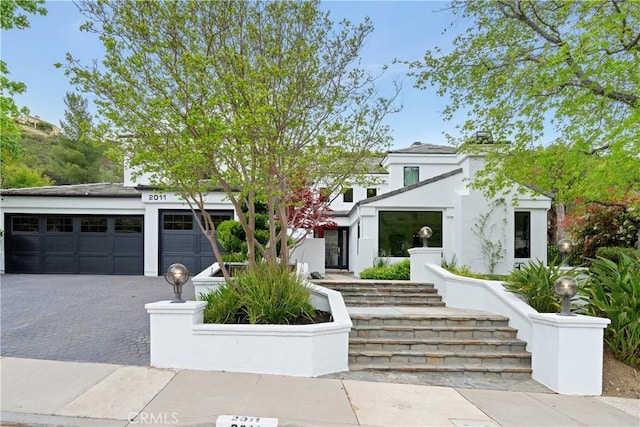 view of front facade featuring stucco siding, decorative driveway, stairs, and an attached garage