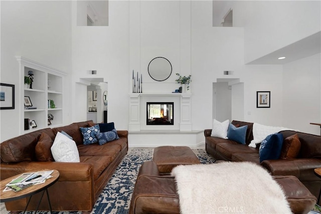 living area with a towering ceiling, a multi sided fireplace, and built in features