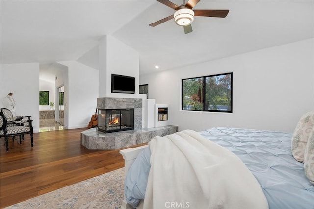 bedroom with a multi sided fireplace, wood finished floors, lofted ceiling, and recessed lighting