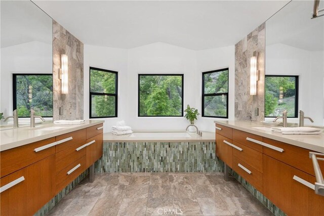 full bathroom with two vanities, a garden tub, vaulted ceiling, and a sink