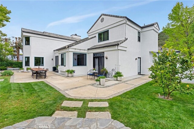 back of property with a lawn, a patio area, and stucco siding
