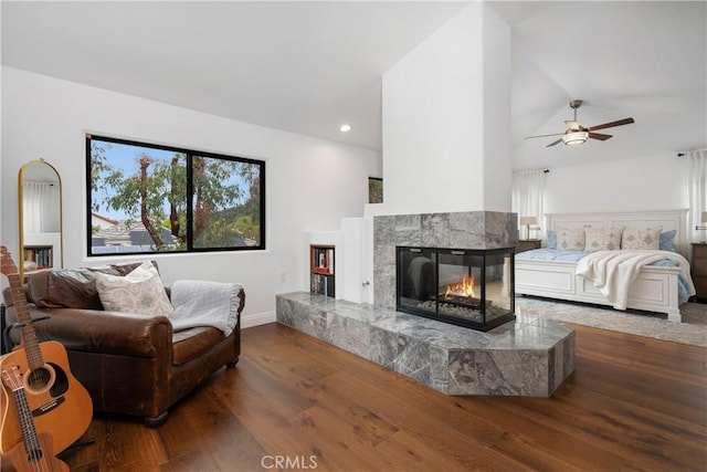living room with wood finished floors, a multi sided fireplace, baseboards, a ceiling fan, and lofted ceiling