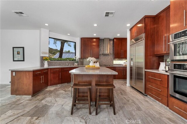 kitchen with visible vents, stainless steel appliances, wall chimney exhaust hood, and a kitchen island
