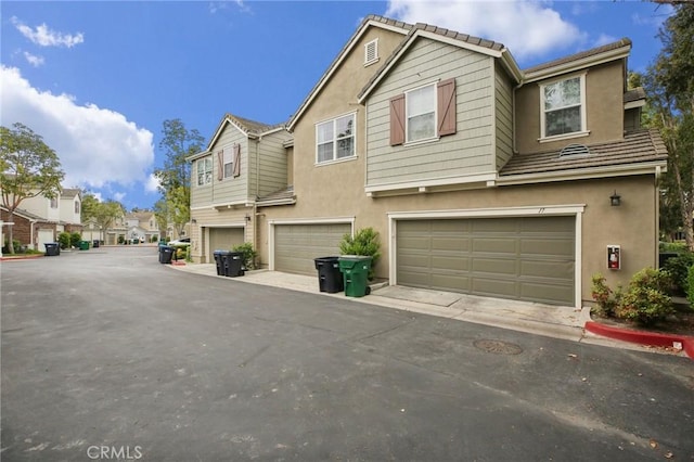 townhome / multi-family property with a residential view, an attached garage, a tile roof, and stucco siding