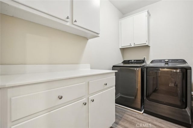 washroom featuring separate washer and dryer, light wood-style floors, and cabinet space