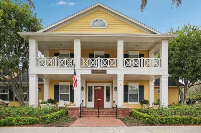 greek revival inspired property with a porch, a balcony, and stucco siding