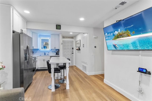 28691 Via Las Flores Unit 328, Murrieta, CA 92563 - kitchen with appliances with stainless steel finishes, light countertops, light wood-style floors, white cabinets, and a breakfast bar