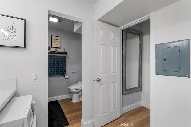 bathroom featuring wood finished floors, toilet, vanity, electric panel, and baseboards