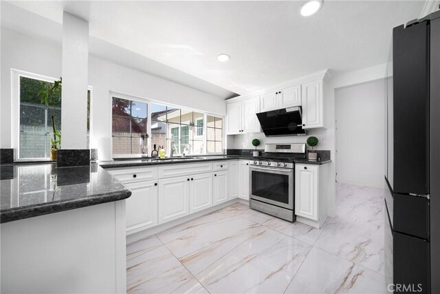 kitchen featuring dark stone counters, freestanding refrigerator, white cabinetry, stainless steel range with gas stovetop, and recessed lighting