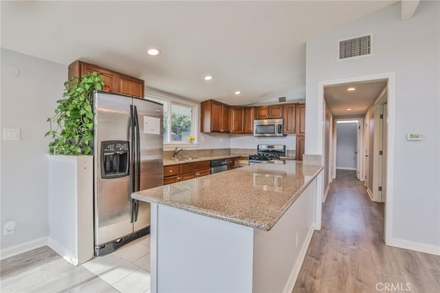 kitchen featuring stainless steel appliances, baseboards, visible vents, light stone counters, and brown cabinetry