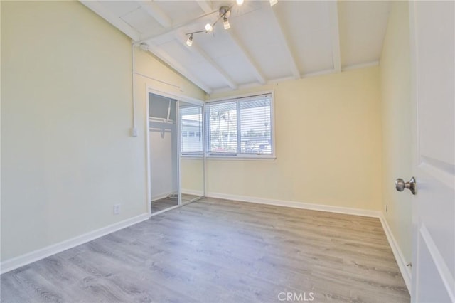 unfurnished bedroom featuring wood finished floors, a closet, vaulted ceiling with beams, and baseboards