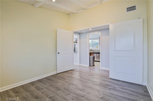 empty room with lofted ceiling with beams, baseboards, wood finished floors, and visible vents