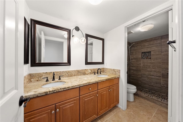 full bathroom with double vanity, toilet, tiled shower, and a sink