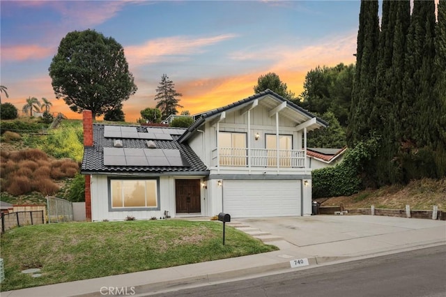 view of front of home featuring concrete driveway, roof mounted solar panels, fence, a front yard, and a garage