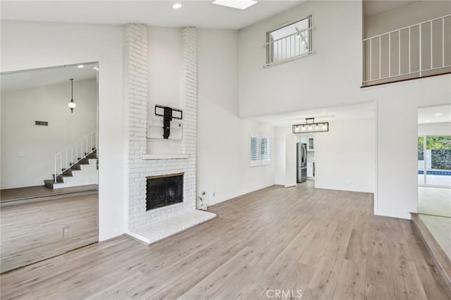 unfurnished living room featuring visible vents, a towering ceiling, wood finished floors, a brick fireplace, and stairs