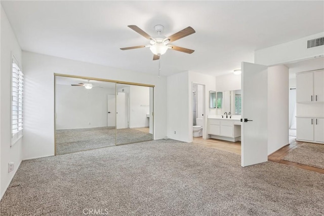 unfurnished bedroom with a ceiling fan, a sink, a closet, light carpet, and visible vents