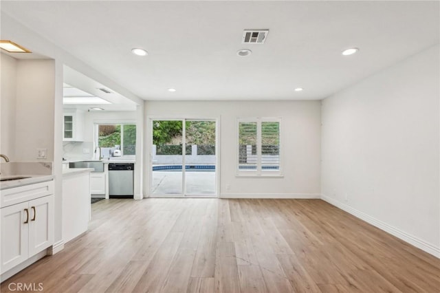 unfurnished living room with visible vents, light wood finished floors, a wealth of natural light, and a sink