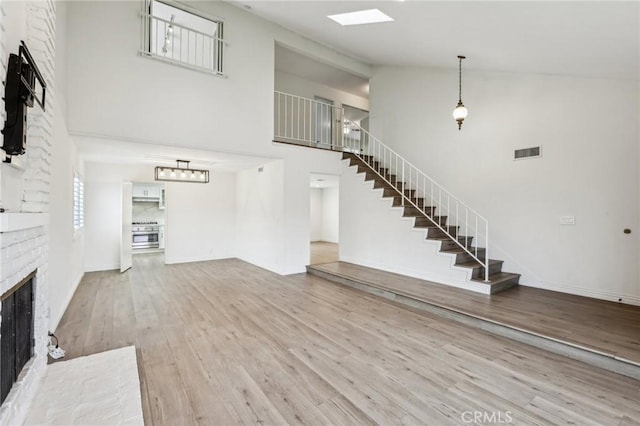 unfurnished living room featuring wood finished floors, visible vents, stairs, a brick fireplace, and high vaulted ceiling