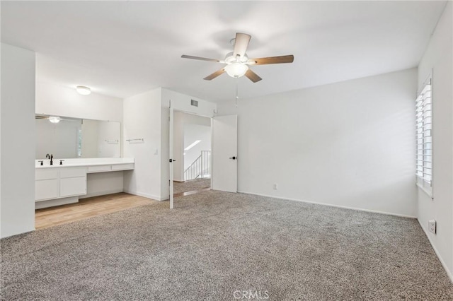 unfurnished bedroom featuring built in desk, multiple windows, light carpet, and a sink
